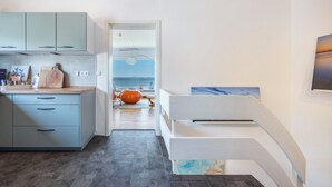 A modern kitchen with light blue cabinets, a wooden cutting board, and a view of the sea through an open door. - Panoramic Lake House at Steinhuder Meer – Your Exclusive Retreat by the Water (Wunstorf)