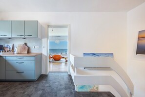 Eine moderne Küche mit hellblauen Schränken, einem Holztisch zum Schneiden und Blick auf das Meer durch eine geöffnete Tür.