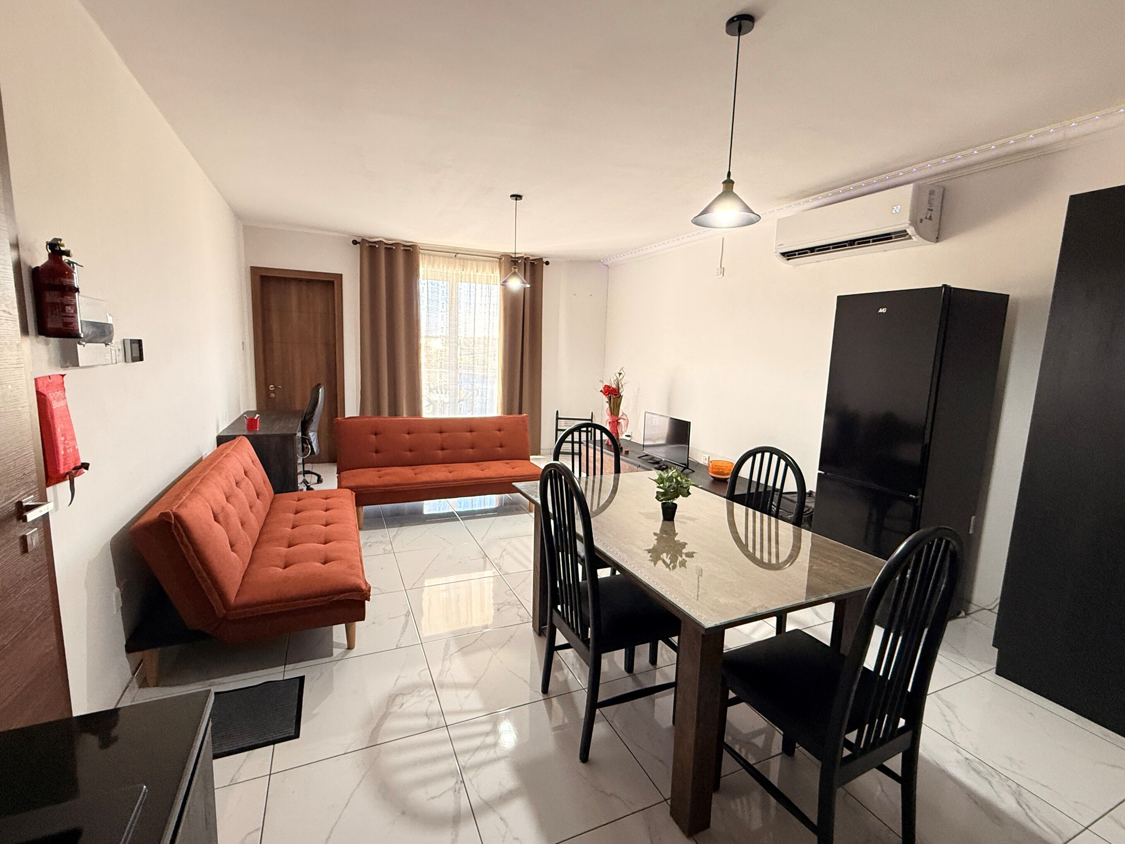 A modern kitchen with a dining table, chairs, a sofa, and a refrigerator.