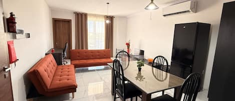 A modern kitchen with a dining table, chairs, a sofa, and a refrigerator.