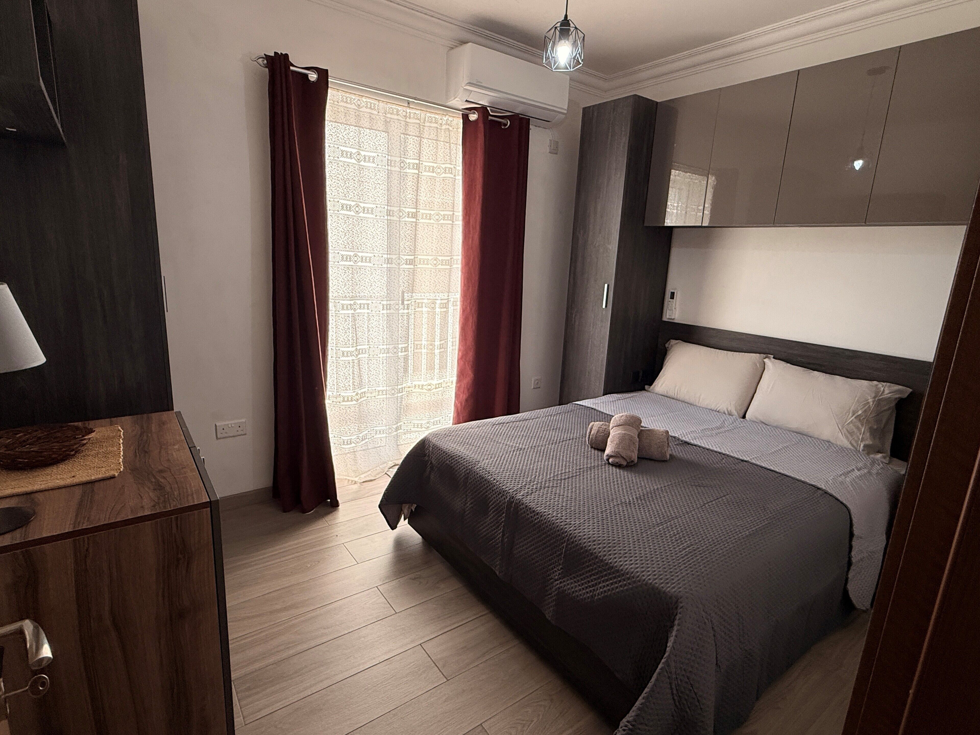 A modern hotel room with a bed, a desk, and a wardrobe.