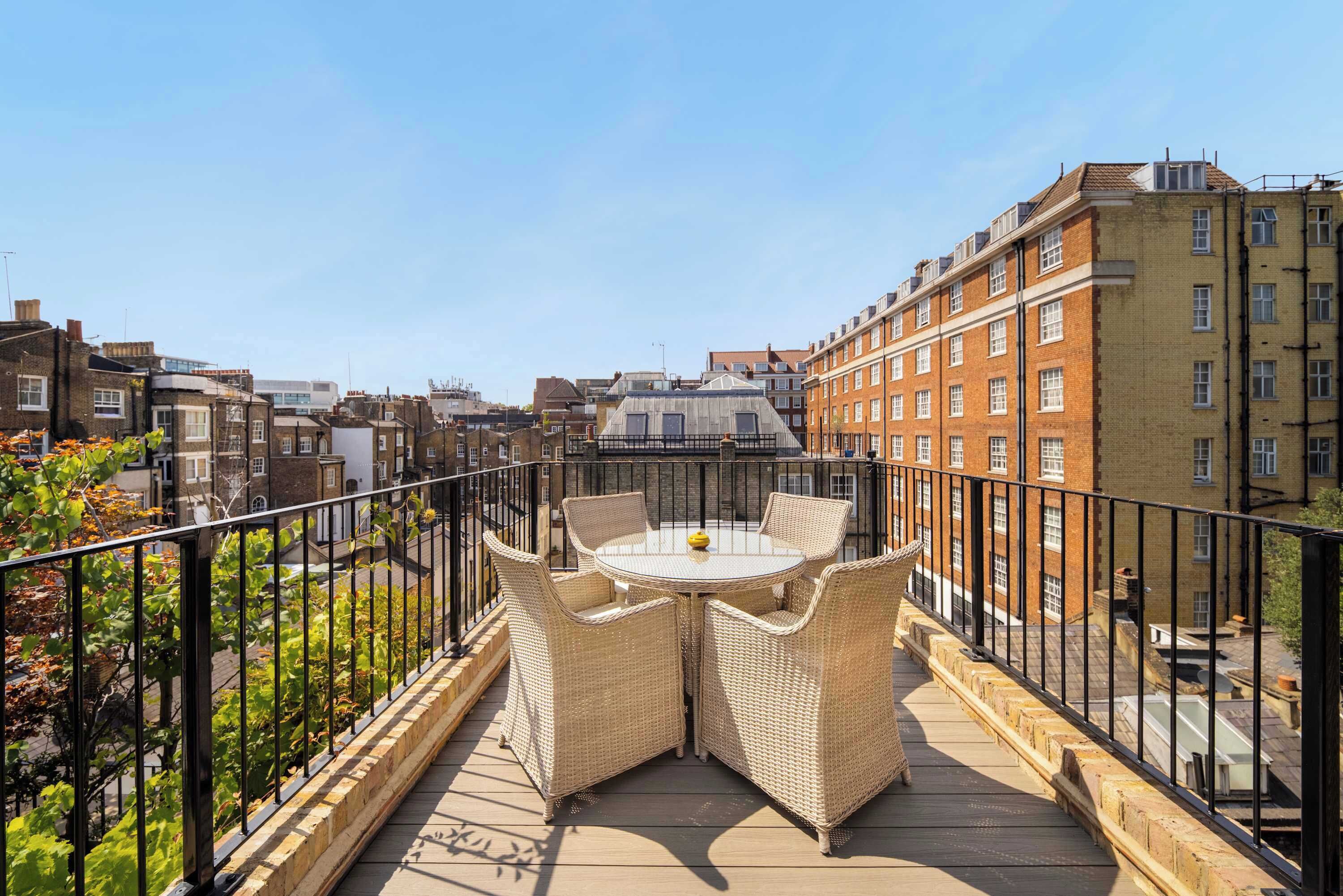 A rooftop terrace with a round table and wicker chairs, surrounded by a metal railing.