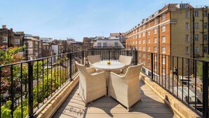 Una terraza en la azotea con una mesa redonda y sillas de mimbre, rodeada por una baranda de metal.