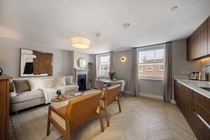 A modern living room with a fireplace, a dining area with a round table, and a kitchen with wooden cabinets. - 6 Mins Walk to Selfridges, Marble Arch Penthouse (Greater London)