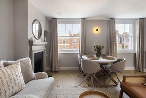 A modern living room with a fireplace, a dining table with chairs, and a view of the city through large windows. - 6 Mins Walk to Selfridges, Marble Arch Penthouse (Greater London)