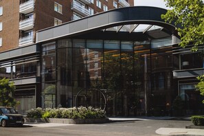 Un bâtiment moderne doté d’une façade en verre incurvée, d’une entrée aménagée et d’un espace de stationnement.