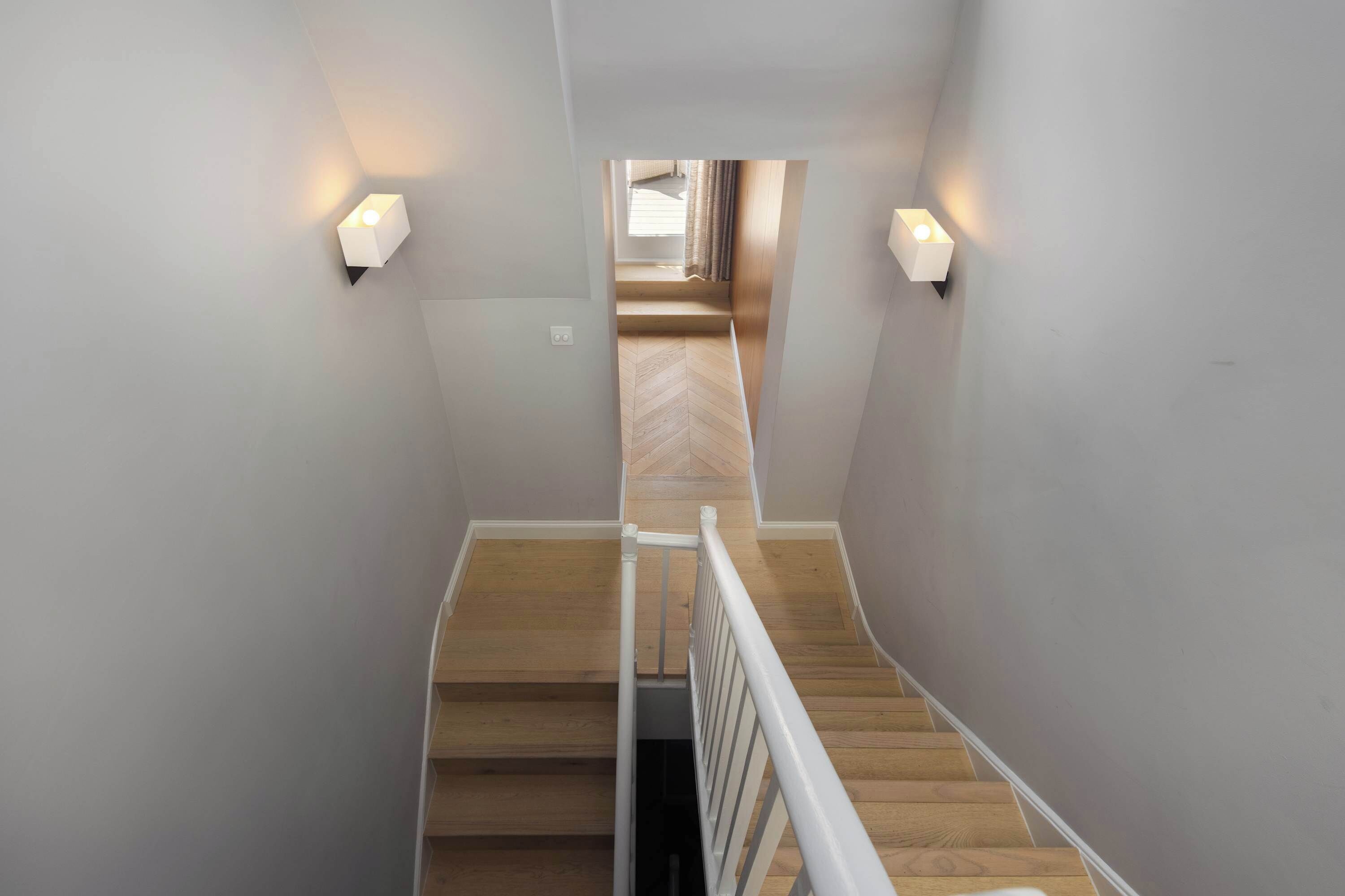 Una escalera de madera con barandillas blancas que conduce a una habitación con piso de espiga.