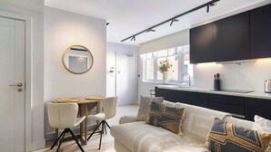 A modern kitchen with dark cabinets, a dining area with a round mirror, and a living room with a sofa and decorative pillows. - 9 Mins Walk to Selfridges, Marble Arch Studio (Greater London)