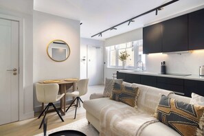 Eine moderne Küche mit dunklen Schränken, ein Essbereich mit rundem Spiegel und ein Wohnzimmer mit Sofa und Zierkissen.