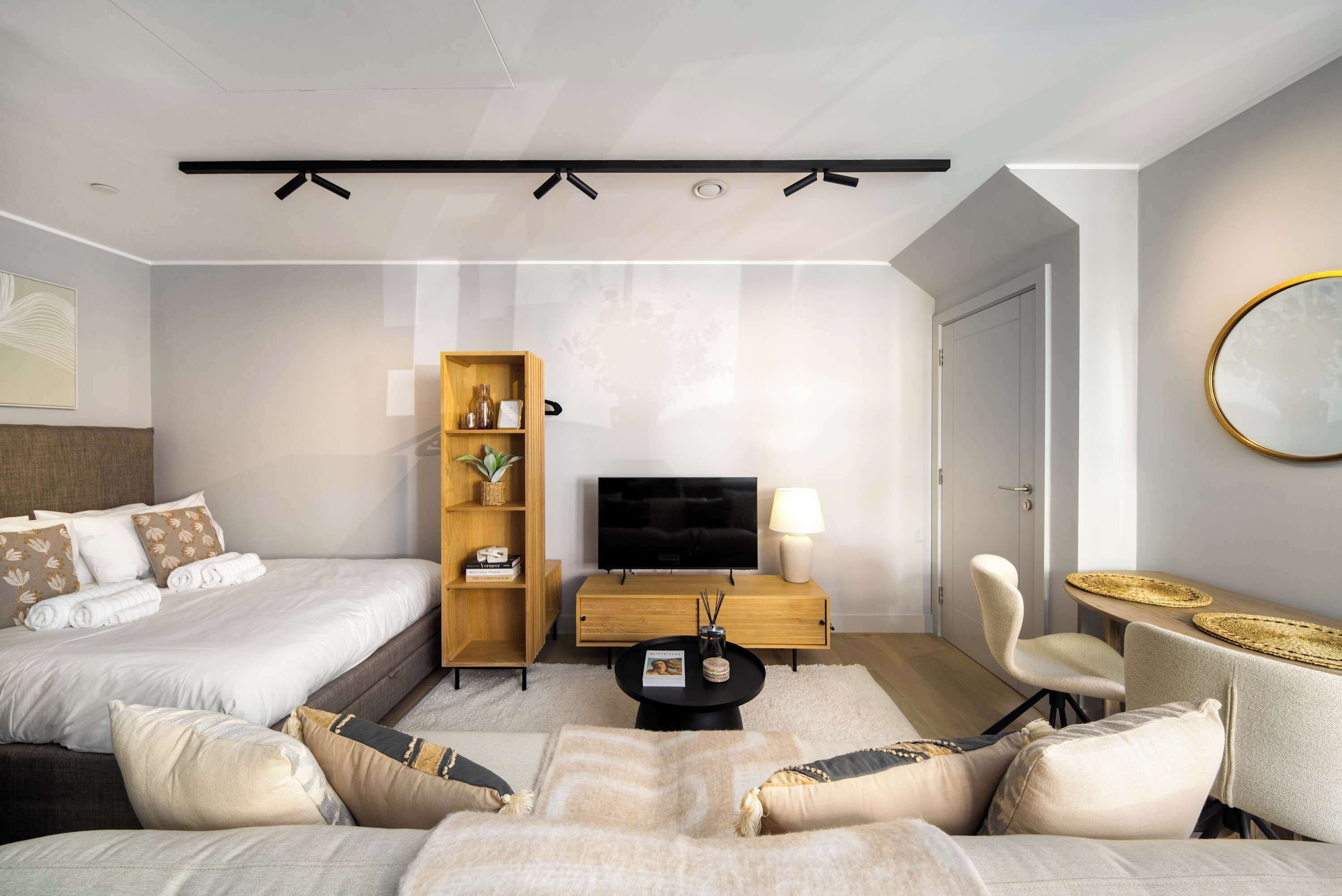 A modern hotel room with a bed, a TV, a seating area, and a bookshelf.