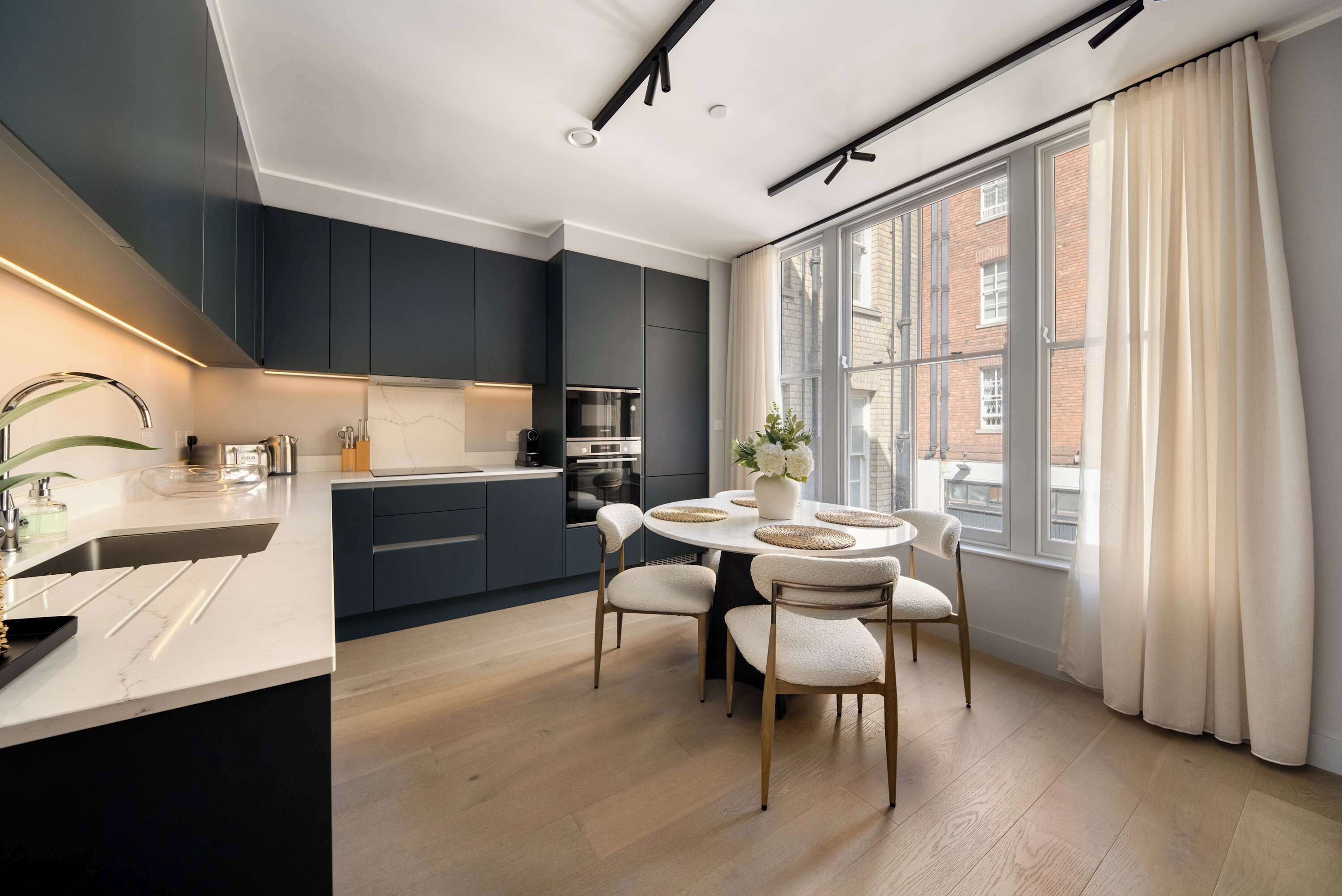 A modern kitchen with dark cabinetry, a central island, and a dining area with a round table and chairs.