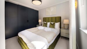 Moderni hotellihuone, jossa on suuri sänky, tumma vaatekaappi, yöpöydällä olevat lamput ja kattovalaisin.