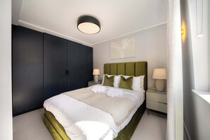 Ein modernes Hotelzimmer mit einem großen Bett, einem dunklen Wandschrank, Nachttischlampen und einer Deckenleuchte.