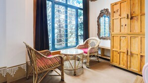 A room with a large window, wicker chairs, a round table, and a wooden cabinet. - Palette Bhatta Falls Formerly Meru Pahad (Mussoorie)
