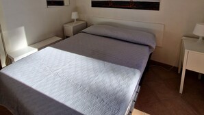 Un dormitorio con cama, mesitas de noche, lámpara colgante, espejo en la pared y ventana.