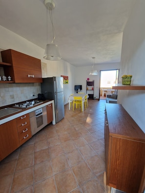 A modern kitchen with a stove, oven, and refrigerator. There is a dining area with a table and chairs. - Apartment 200 meters from the beach with free parking (San Vito Lo Capo)