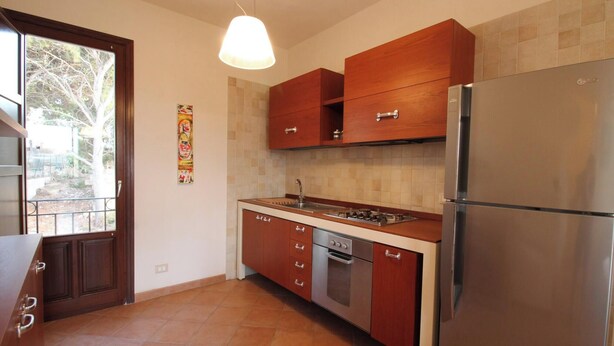 Una cocina con armarios de madera, un refrigerador de acero inoxidable, horno empotrado y una lámpara colgante.