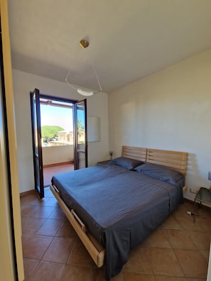 A bedroom with a bed, a nightstand, a lamp, and a view through an open door. - Apartment 200 meters from the beach with free parking (San Vito Lo Capo)