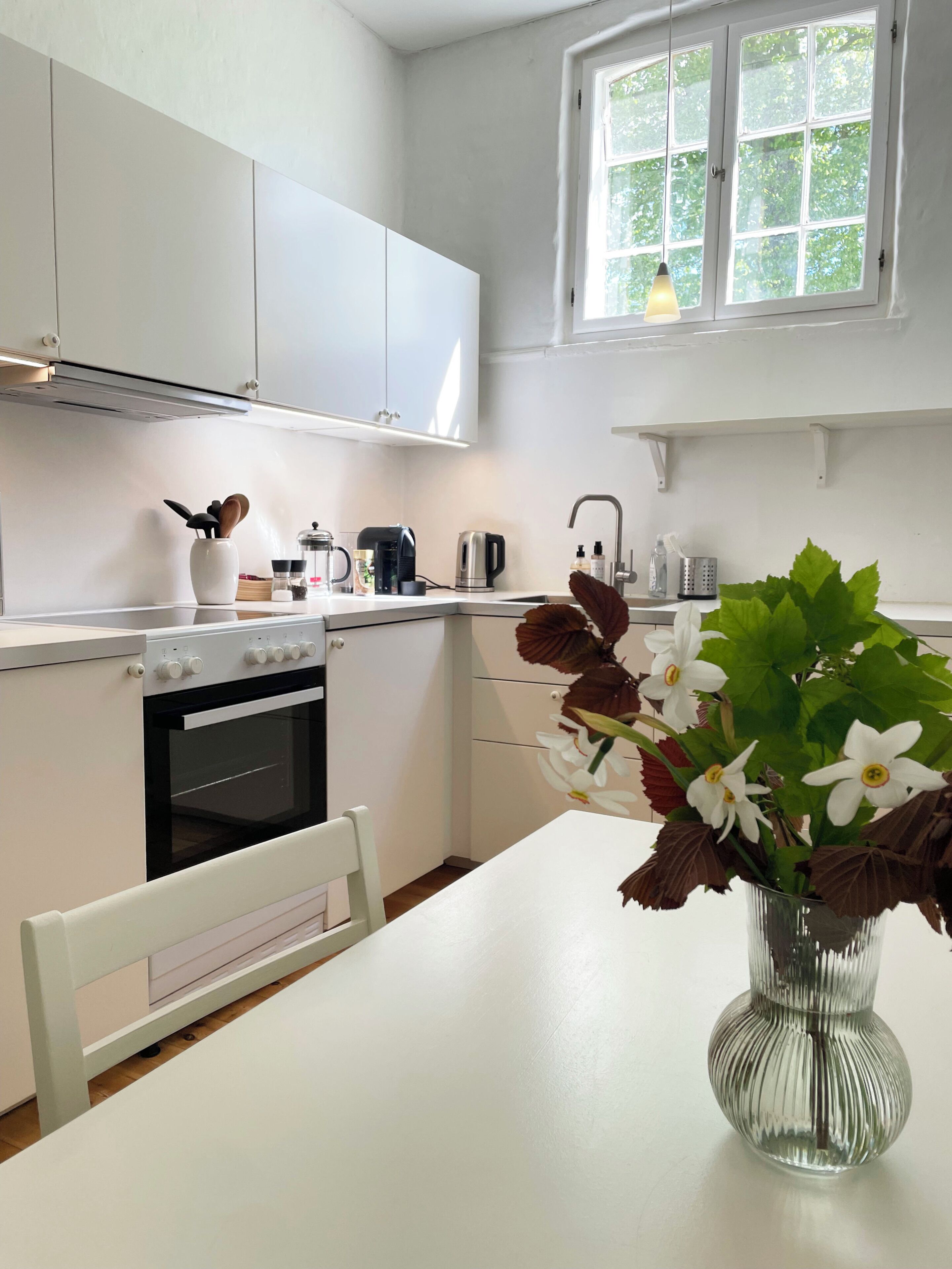 A modern kitchen with white cabinets, a stove, and a window with a view of greenery.