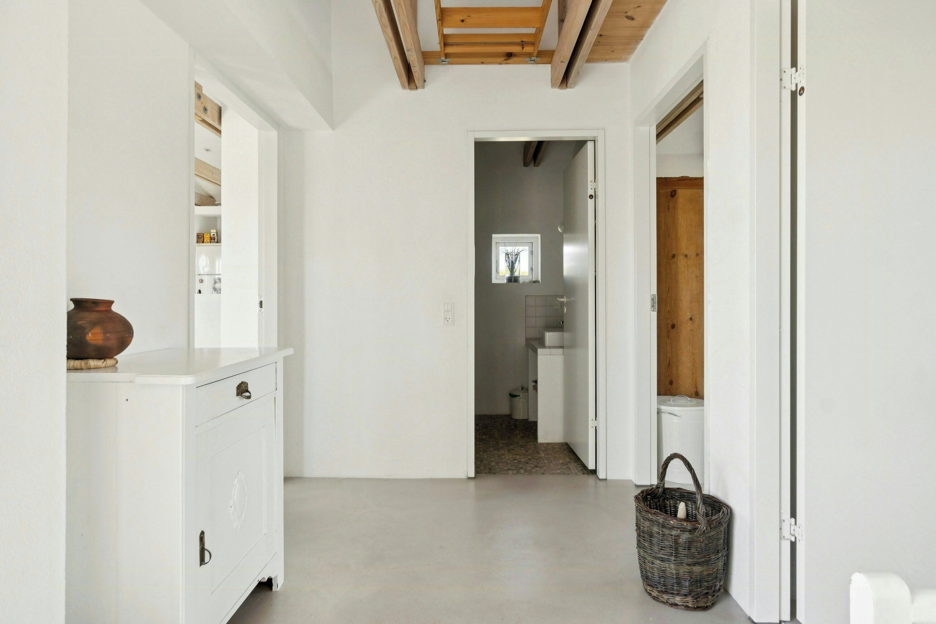 A narrow hallway with a white cabinet on the left, a wicker basket on the floor, and a wooden door on the right.