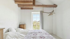 Ein Schlafzimmer mit einem Bett, einem Holz-Kopfteil, einem Nachttisch, einem Fenster mit Vorhängen und Blick ins Freie.