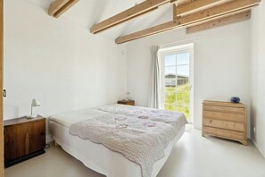A bedroom with a bed, a nightstand, a dresser, and a window with a view. - Summer cottage with grass roof in Klitmøller (Thisted)