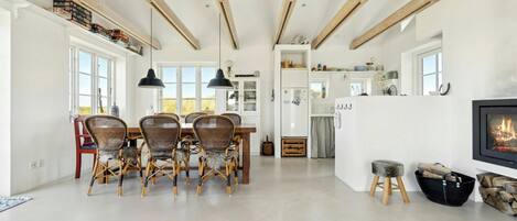 Amplia sala de estar con una mesa de comedor, sillas, chimenea y una cocina al fondo.