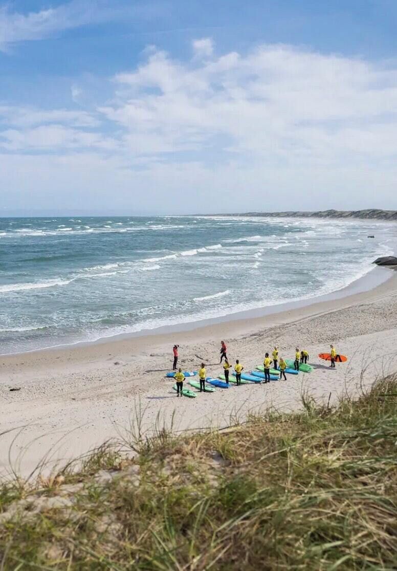 A beach with people in yellow shirts standing on the sand, some holding surfboards.