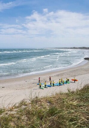 A beach with people in yellow shirts standing on the sand, some holding surfboards. - Summer cottage with grass roof in Klitmøller (Thisted)