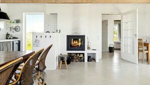 Eine moderne Küche mit weißen Schränken, eine Essecke mit Korbstühlen, ein Kamin und eine Holzbalkendecke.