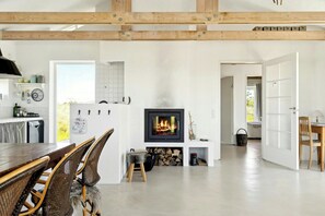 Eine moderne Küche mit weißen Schränken, eine Essecke mit Korbstühlen, ein Kamin und eine Holzbalkendecke.