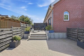 Ein Innenhof mit einem Backsteinhaus, einem Holzzaun und Sitzgelegenheiten im Freien.