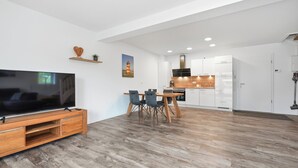 Ein modernes Wohnzimmer mit Flachbildfernseher, einer Holz-Unterhaltungseinheit und einem Essbereich mit Tisch und Stühlen.