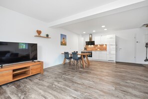 Ein modernes Wohnzimmer mit Flachbildfernseher, einer Holz-Unterhaltungseinheit und einem Essbereich mit Tisch und Stühlen.