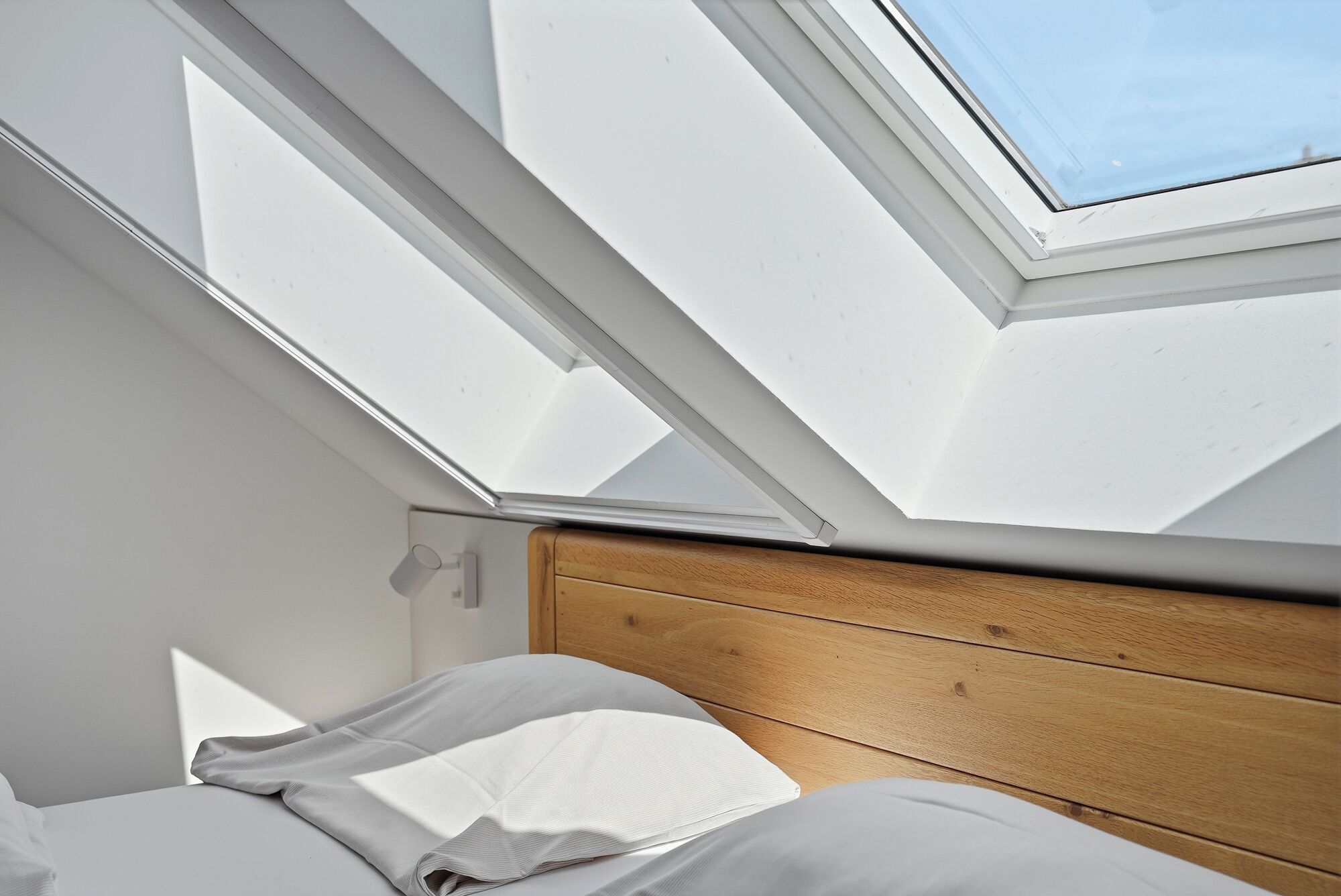 A room with a skylight, wooden headboard, and a bed with white bedding.
