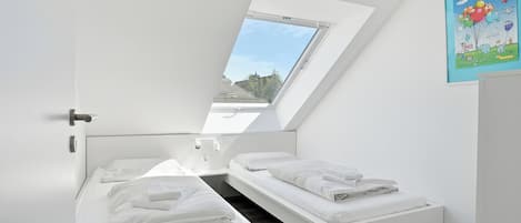 A bedroom with two beds, a skylight, and a painting on the wall.