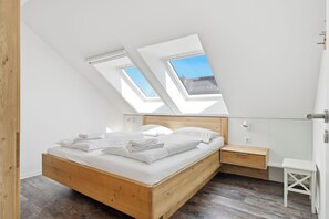 Ein Schlafzimmer mit Dachfenster, einem hölzernen Bett, einem Nachttisch und einem kleinen weißen Stuhl.