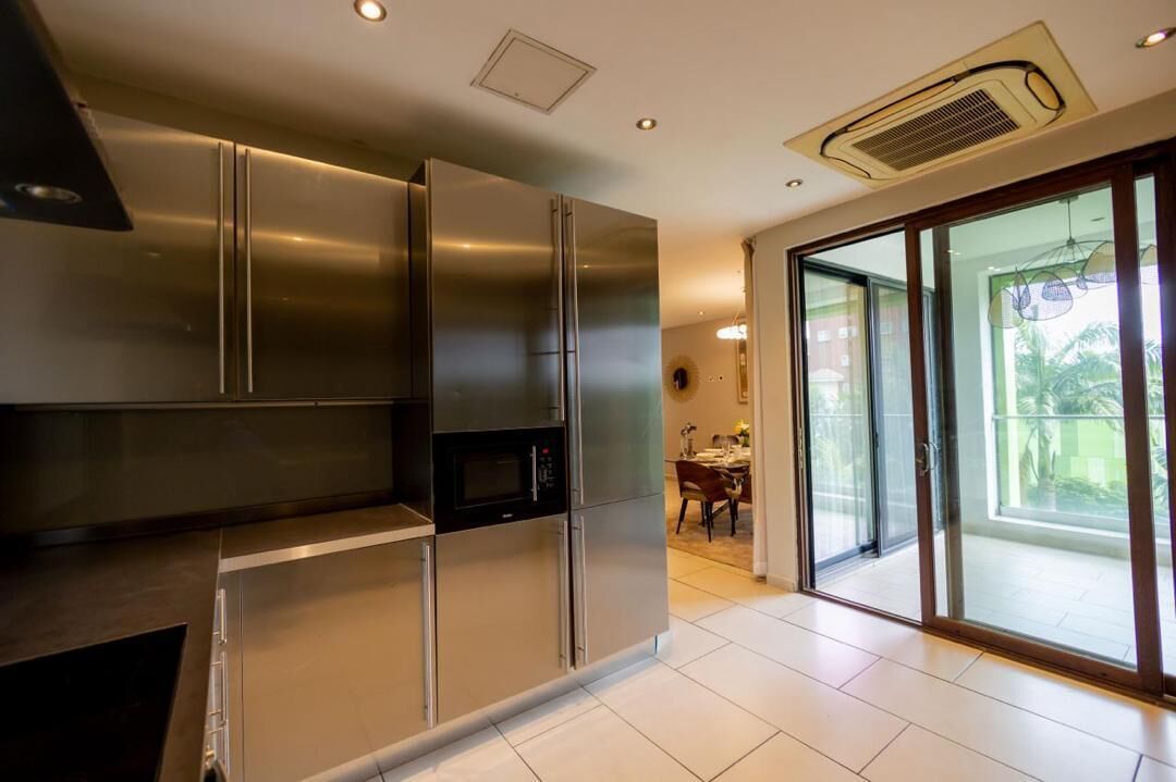A modern kitchen with stainless steel appliances, a dining area with a table and chairs, and a sliding glass door leading to a balcony.