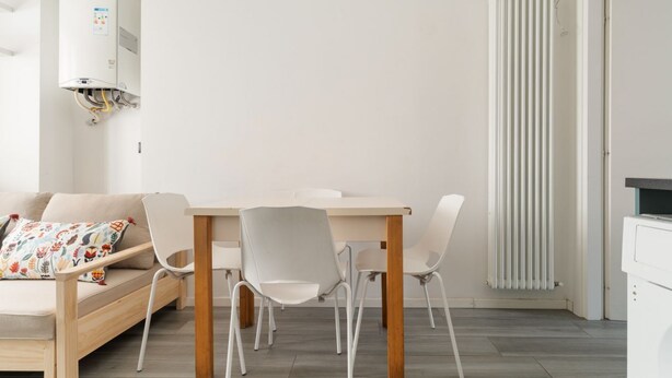 Ein modernes Wohnzimmer mit Sofa, Esstisch, Stühlen, einer Heizung und einem weißen Heizlüfter.