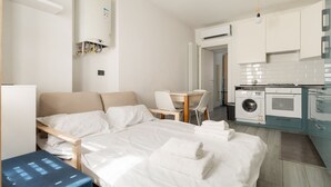 Ein kleines Hotelzimmer mit Bett, Schreibtisch, Stuhl, Waschmaschine und einer Küchenzeile.