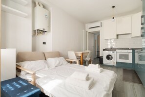 Ein kleines Hotelzimmer mit Bett, Schreibtisch, Stuhl, Waschmaschine und einer Küchenzeile.