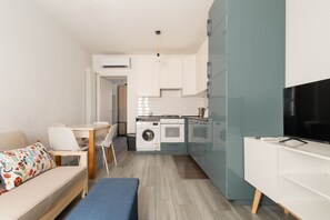 Eine kompakte Küche mit Waschmaschine, einem Essbereich mit einer Bank und einem Fernseher auf einem Standfuß.