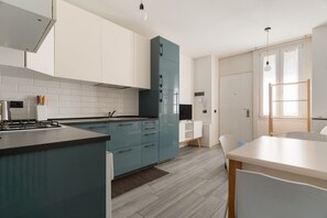 Una cuina moderna amb armaris blancs, una illa color cel i una zona menjador amb taula i caires blancs.