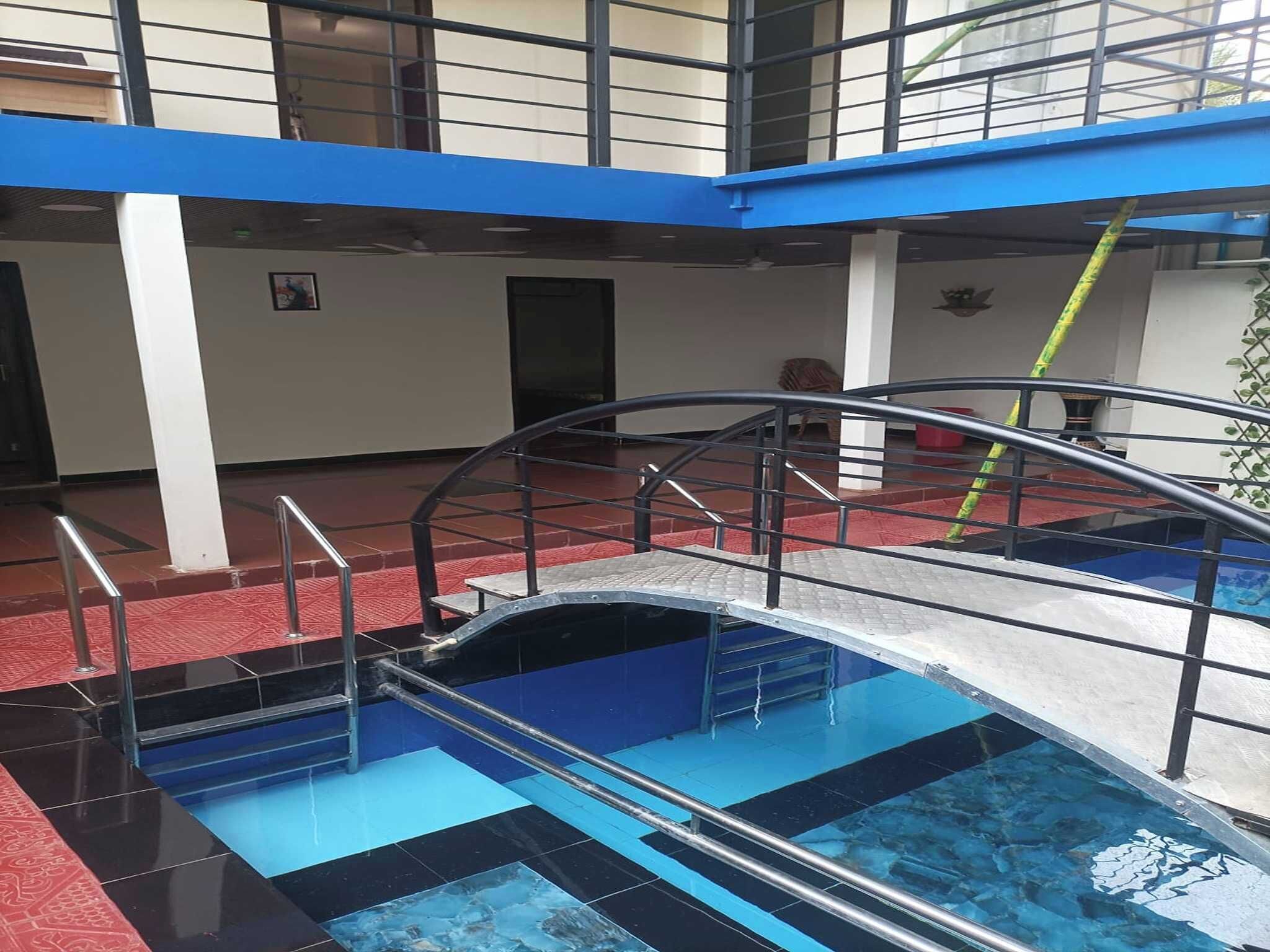 A swimming pool with a metal bridge and railings, surrounded by a red floor and blue walls.