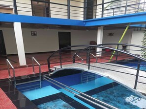A swimming pool with a metal bridge and railings, surrounded by a red floor and blue walls. - Palette Rajas Paradise Villa 3BHK Pool (Madurai)