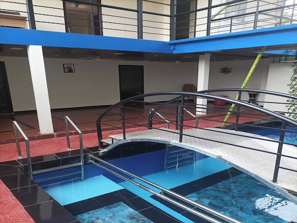 A swimming pool with a metal bridge and railings, surrounded by a red floor and blue walls.