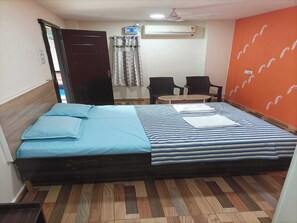 A room with a bed, two chairs, a small table, an air conditioning unit, and a door.