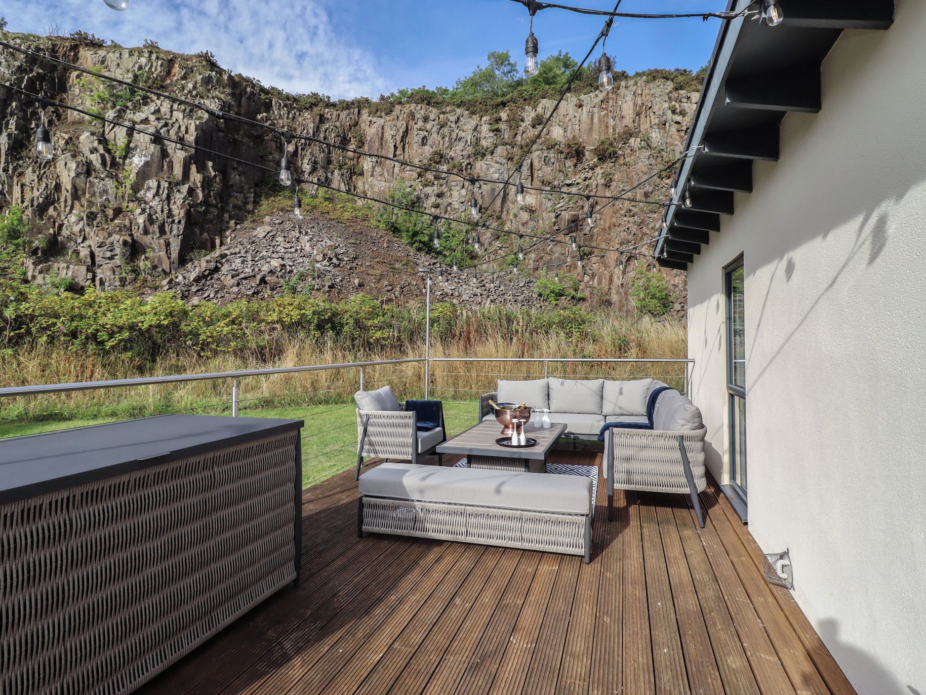 Um deck externo com um conjunto de sofás, uma mesa e um espaço bar.