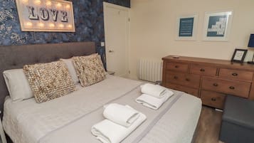 Una cama bien hecha con almohadas, una mesita de noche, un aparador y una pared con un letrero que dice 'LOVE' y cuadros enmarcados.