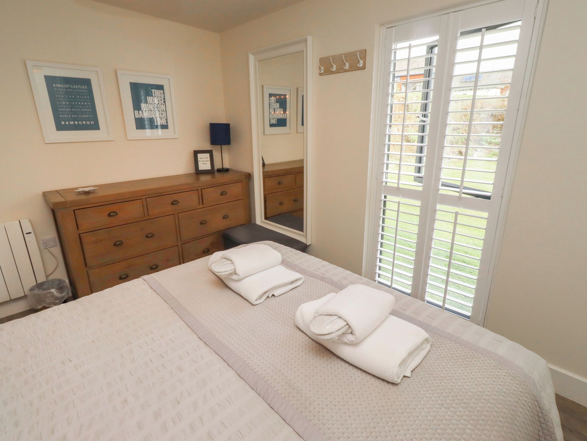 A bedroom with a bed, a dresser, a mirror, and a window with blinds.
